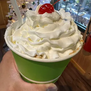 a hand holding a cup of ice cream with a cherry on top