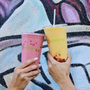 two people holding drinks in front of a graffiti wall