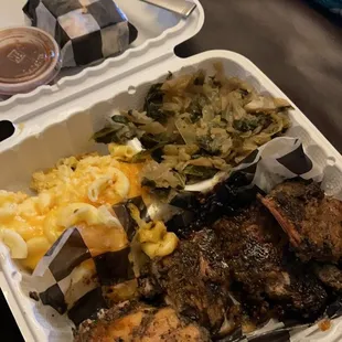 Jerk chicken dinner with sides of Mac-n-cheese and collard green/cabbage mix.