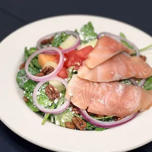 a salad with salmon, lettuce, tomatoes, and pecans