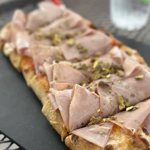 a piece of bread with ham and pistachios