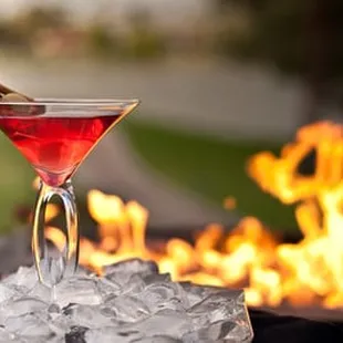 a cocktail in a martini glass on ice with flames in the background