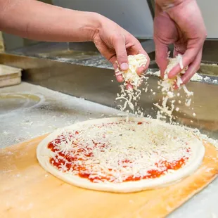a person sprinkling cheese on a pizza
