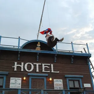 Stunt Performer leaps from the top of the Hotel while clutching a flag.