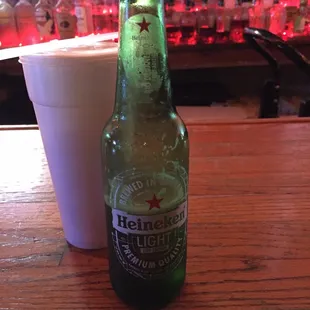 a bottle of heineken beer next to a white cup