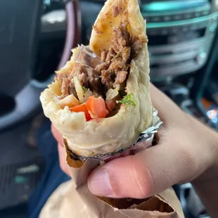 a hand holding a pita filled with meat and vegetables