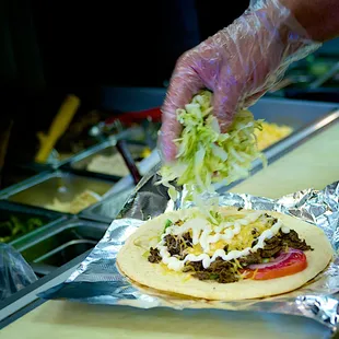 a person putting toppings on a pita