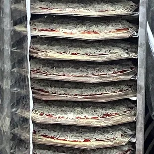 large pizzas stacked to be dressed &amp; hit the oven