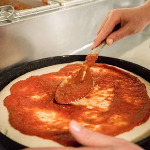 a person putting sauce on a pizza