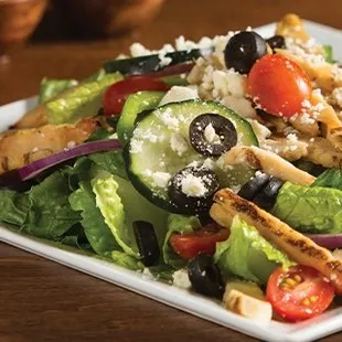 a salad with chicken, cucumbers, tomatoes, black olives, and feta cheese