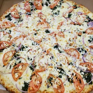 a pizza with tomatoes, onions, and spinach