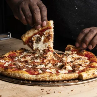 a person taking a slice of pizza