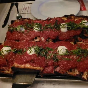 a square pizza covered in sauce and toppings