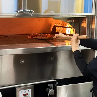 a woman putting a pizza into an oven