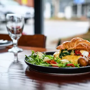 Breakfast croissant with poached egg, side of potatoes and salad.