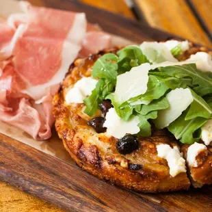 a pizza topped with cheese, arugula, and prosciutto