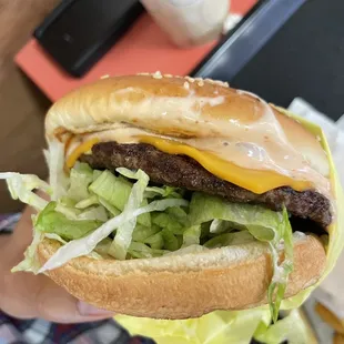 a hand holding a hamburger with lettuce and cheese