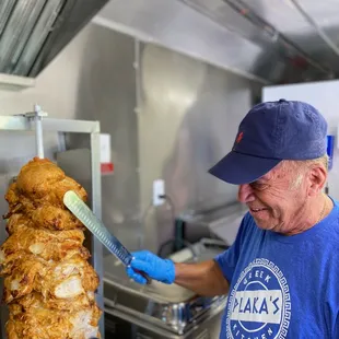 a man in a blue shirt and blue hat cooking a large piece of chicken