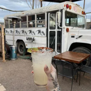 a person holding a margarita in front of a bus