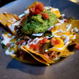 Chicken Tinga Nachos - house made chips, tomatoes, jalapenos, sour cream, cheese sauce. Guacamole is extra.