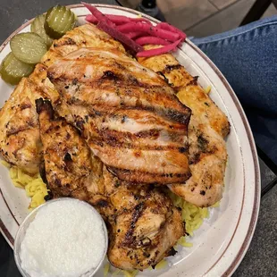 a plate of grilled chicken with a side of pickles