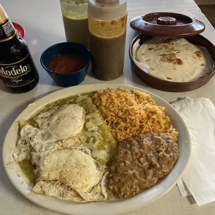 Cheese enchiladas with verde sauce topped with fried eggs. Accompanied by refried beans, rice, and flour tortillas.