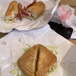 two sandwiches on paper on a picnic table