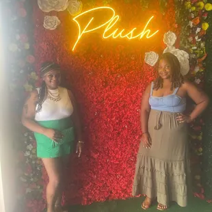 two women standing in front of a floral wall