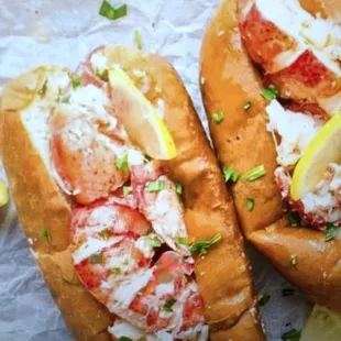 two lobster sandwiches with lemon wedges