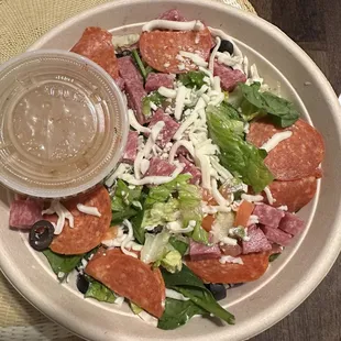 a salad with pepperoni, lettuce, olives, and cheese