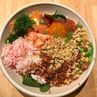 Poke bowl with spring greens, salmon, tuna, crab, seaweed salad, corn, carrots, edamame