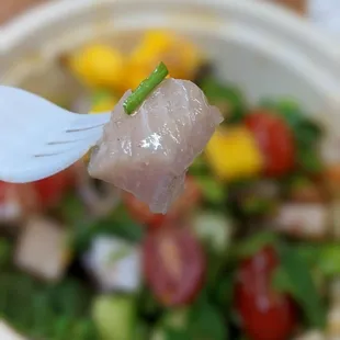 a piece of meat on a fork over a salad