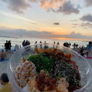 a person holding a plastic bowl of food on the beach