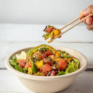 a person holding chopsticks over a bowl of salad
