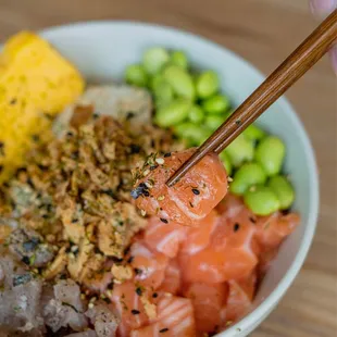 a person holding chopsticks over a bowl of food