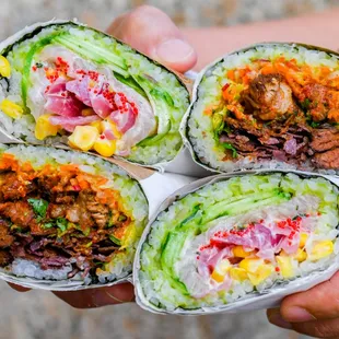a hand holding three burritos