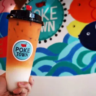 a hand holding a drink in front of a mural