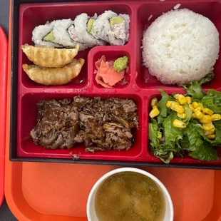 a bento box with rice, meat and vegetables