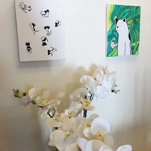 a vase of white orchids in front of paintings