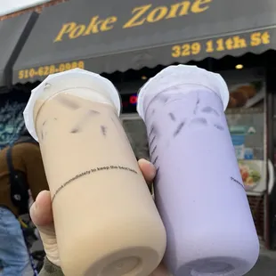 a hand holding two drinks in front of a store