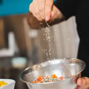 a person sprinkling salt into a bowl of vegetables