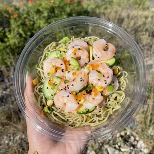 a person holding a bowl of noodles with shrimp and avocado