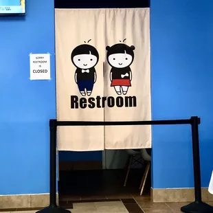 a woman and a man standing in front of a restroom sign