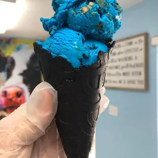 a hand holding a cone of blue ice cream