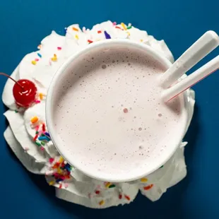 a cup of milkshake with sprinkles and a cherry