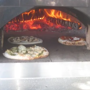 two pizzas cooking in a brick oven