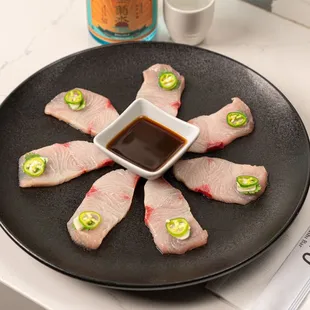 Our Hamachi Jalapeño - Delicately sliced yellowtail topped with garlic, cilantro, and jalapeño, served with yuzu dressing.