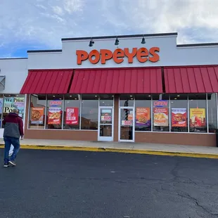 a man walking in front of a popeyes restaurant