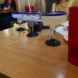 a woman sitting at a table with two margaritas