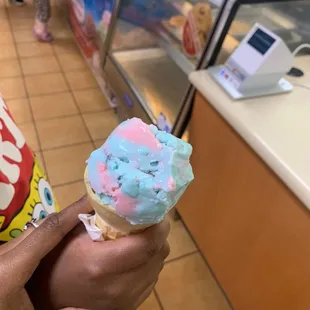 a person holding a cone with blue and pink frosting